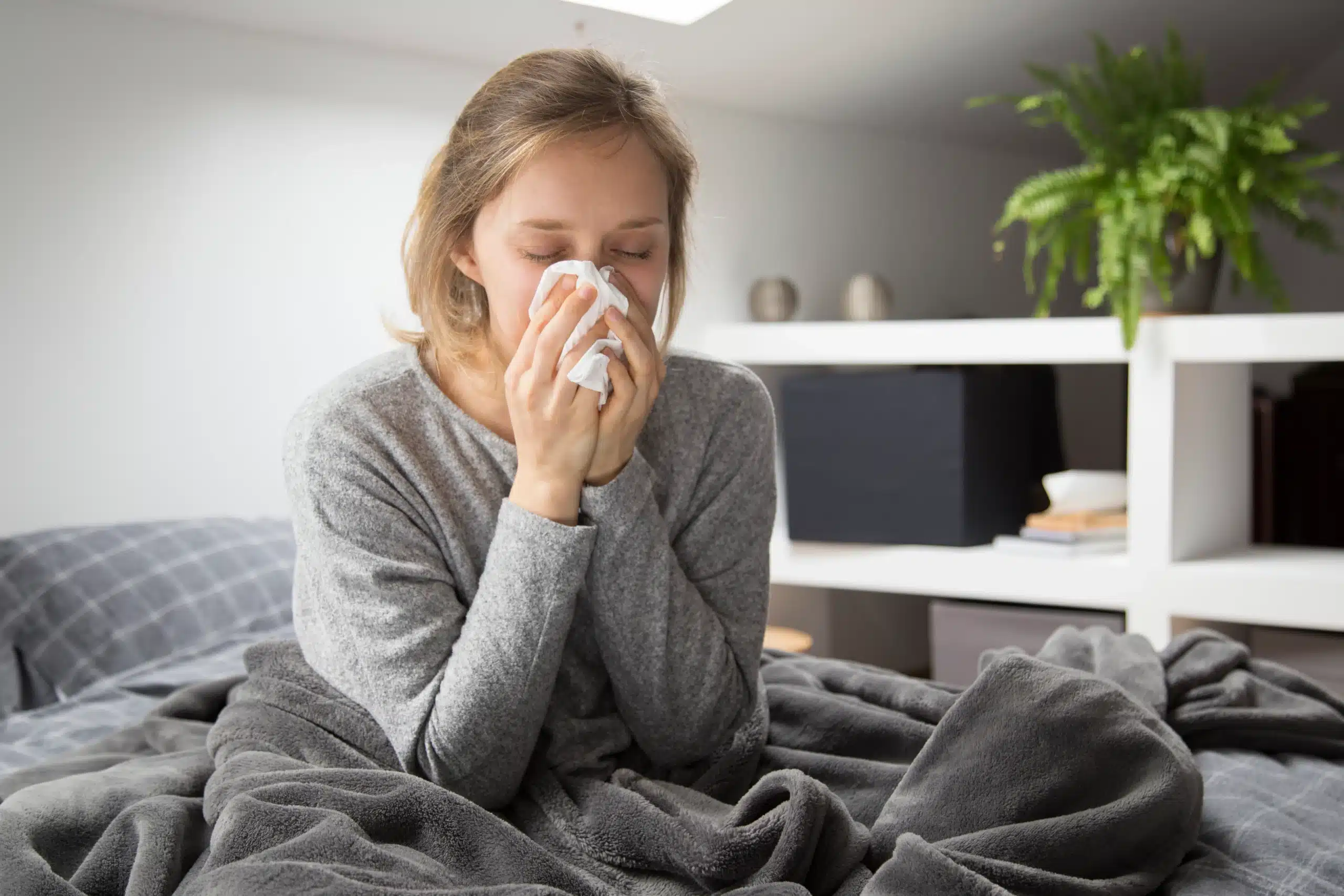 Woman sitting in bed blowing her nose, in need of a cold and flu IV drip at home in Bali