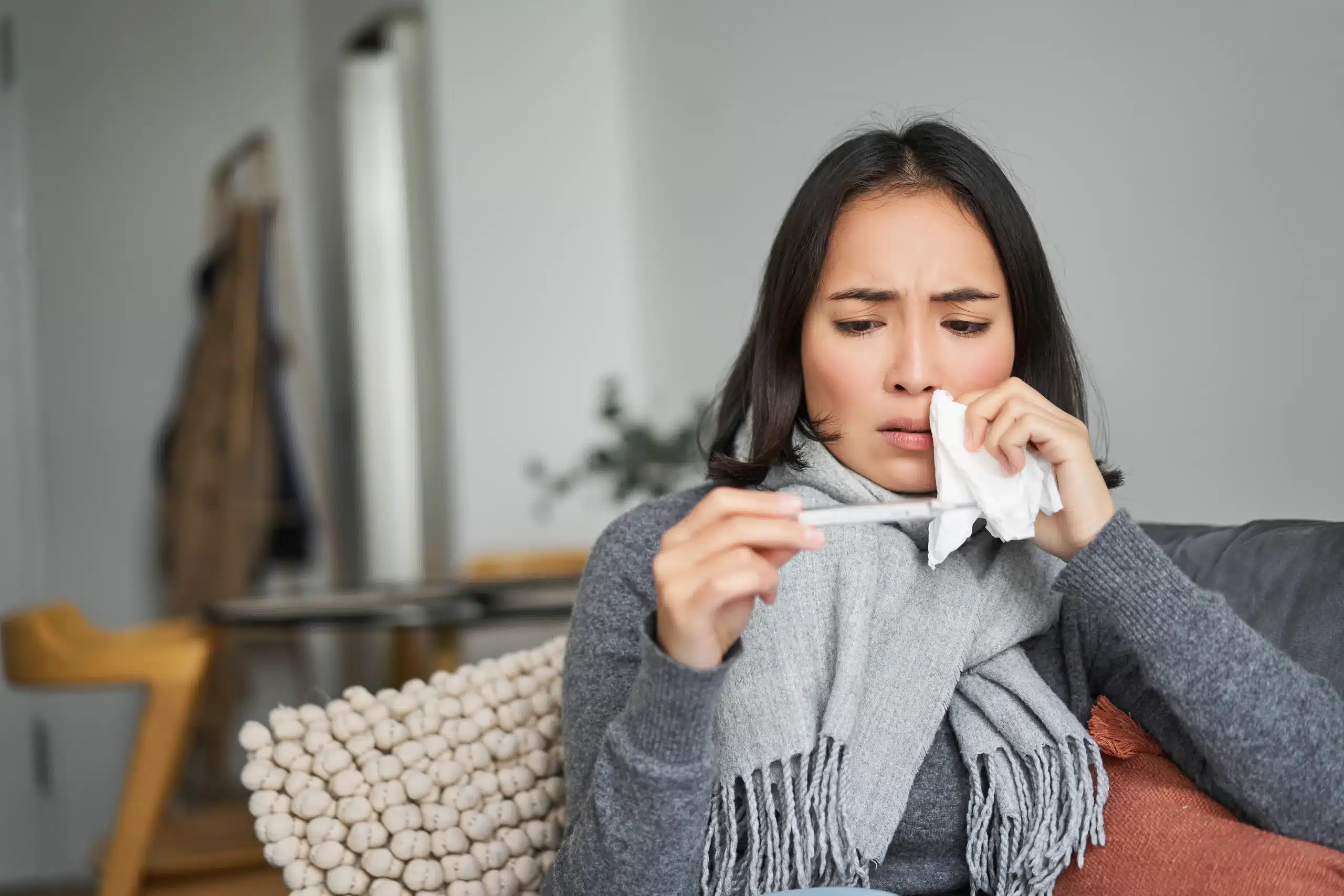 Woman with a fever checking her thermometer on the sofa, in need of a fever IV drip at home in Bali