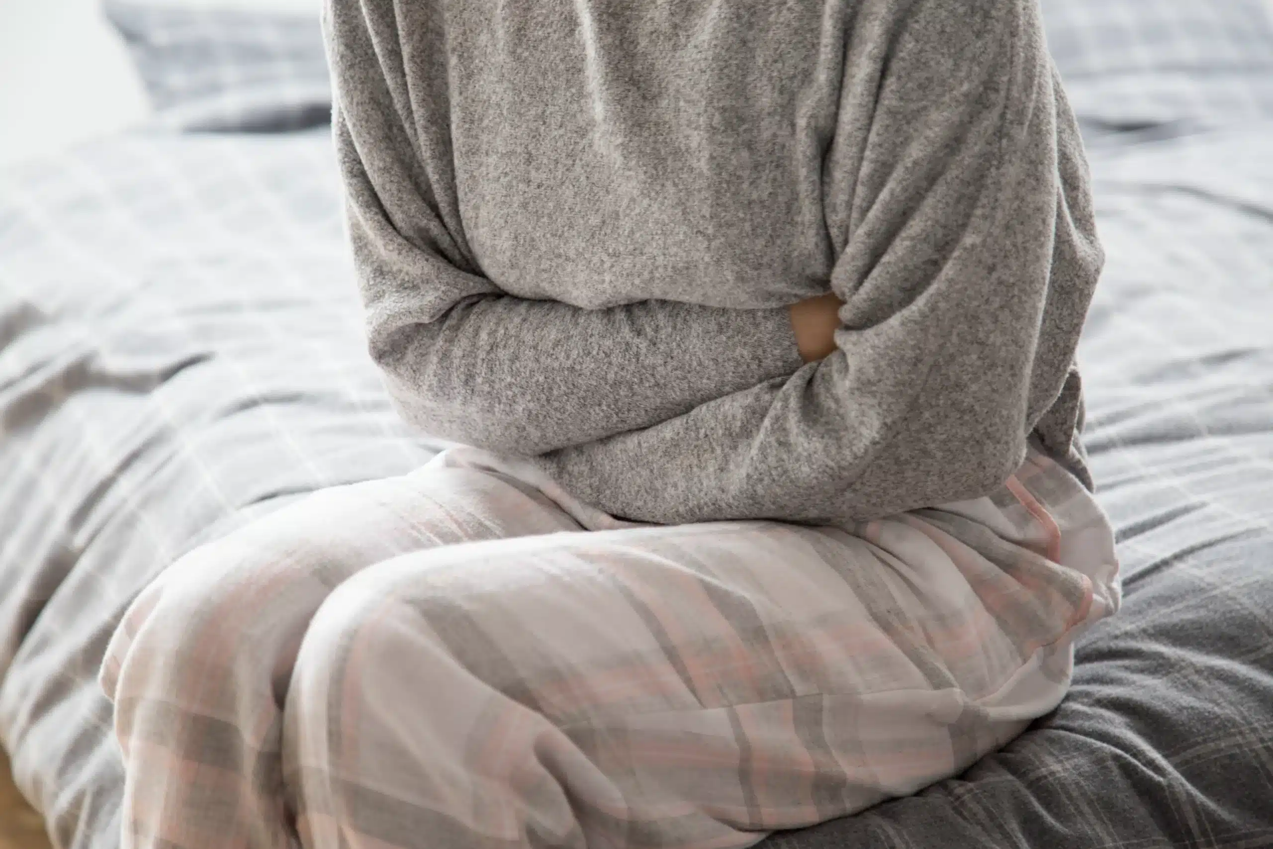 Woman sitting on a bed holding her stomach, in need of food poisoning treatment