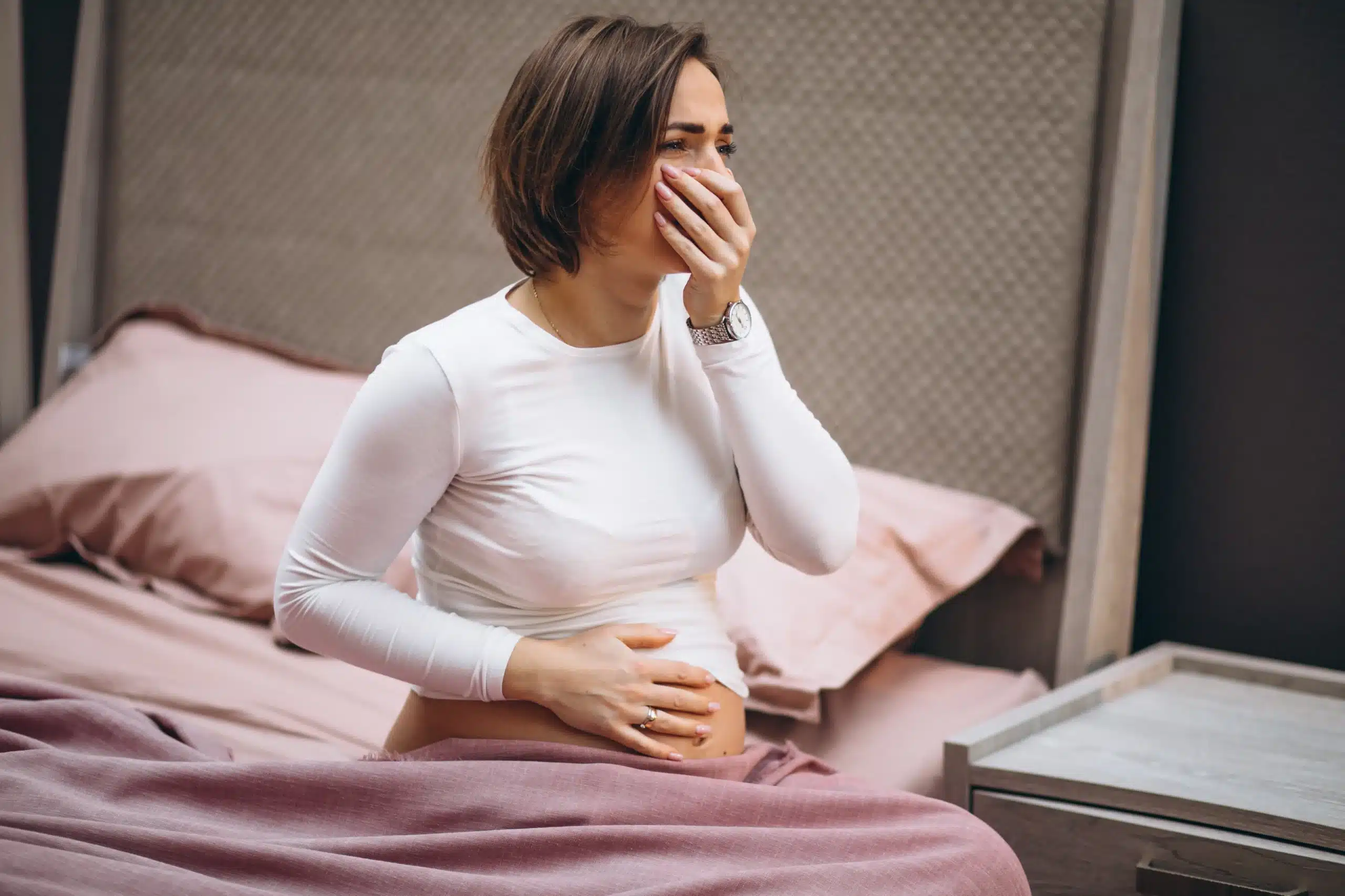 Pregnant woman sitting on her bed covering her mouth with nausea, in need of a morning sickness IV drip in Bali